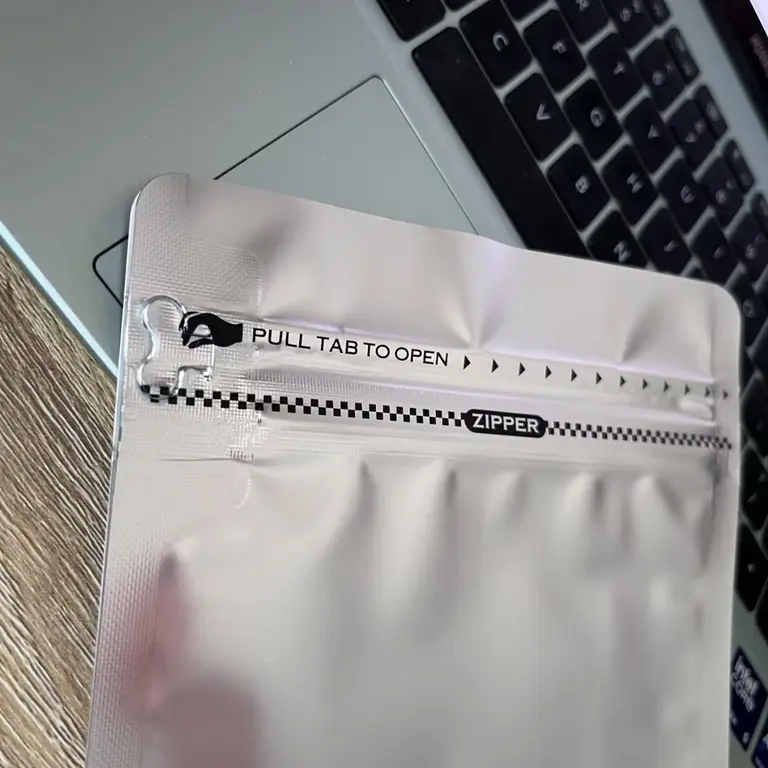 Pull-tab opening and resealable zipper detail on a silver coffee pouch